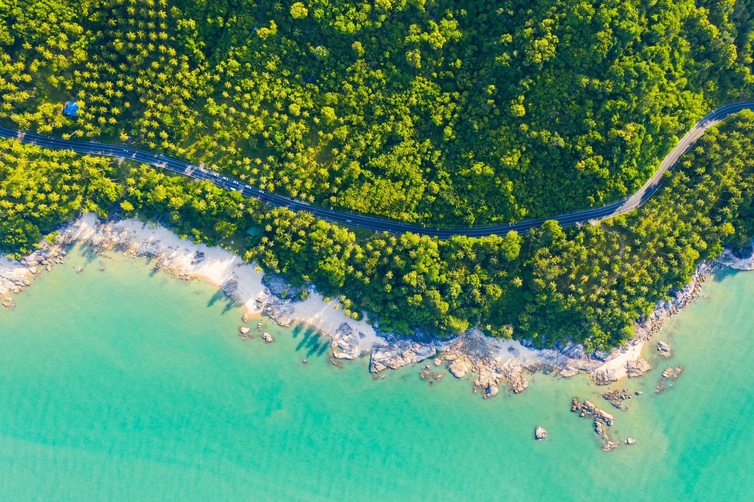 Aerial view of a coastal road winding along Phuket's turquoise shoreline